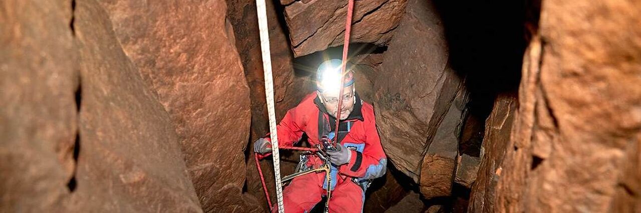 Ein Bergretter seilt sich in eine Höhle ab.