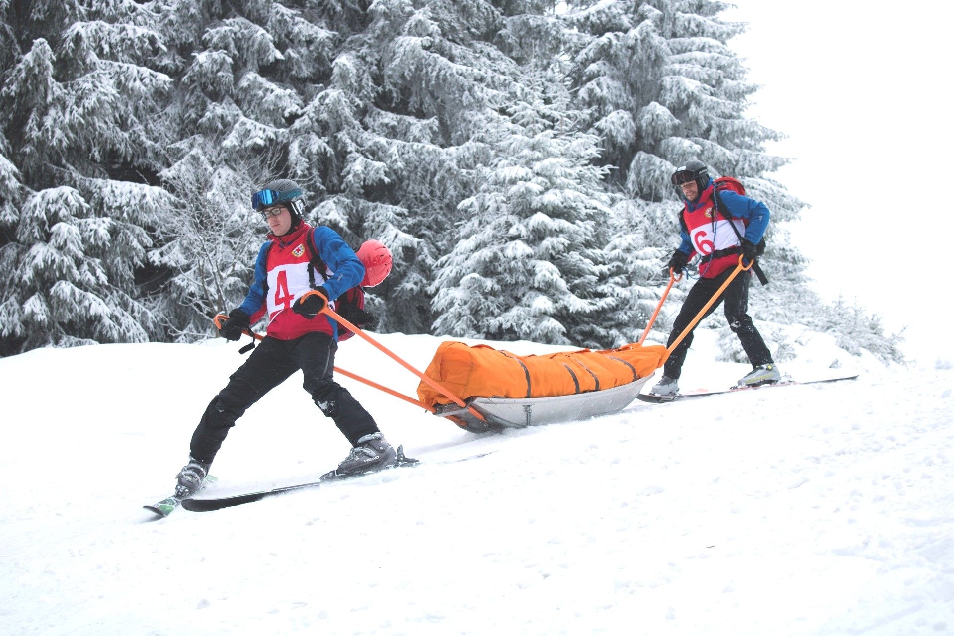 Zwei Retter der Bergwacht transportieren eine verletzte Person in einem Transportschlitten einen Schneehügel hinab. 