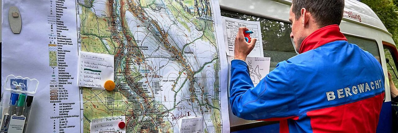 Ein Bergretter trägt Daten in eine Landkarte ein.