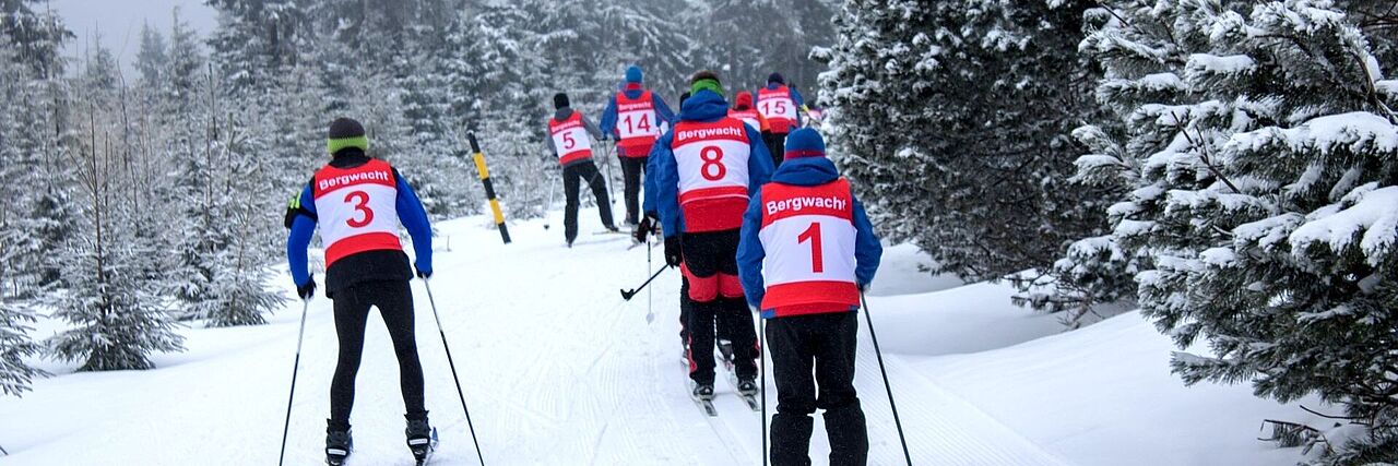 Die Ehrenamtlichen der Bergwacht trainieren ihre Skifahrt-Fähigkeiten und fahren in großer Gruppe durch einen Wald.