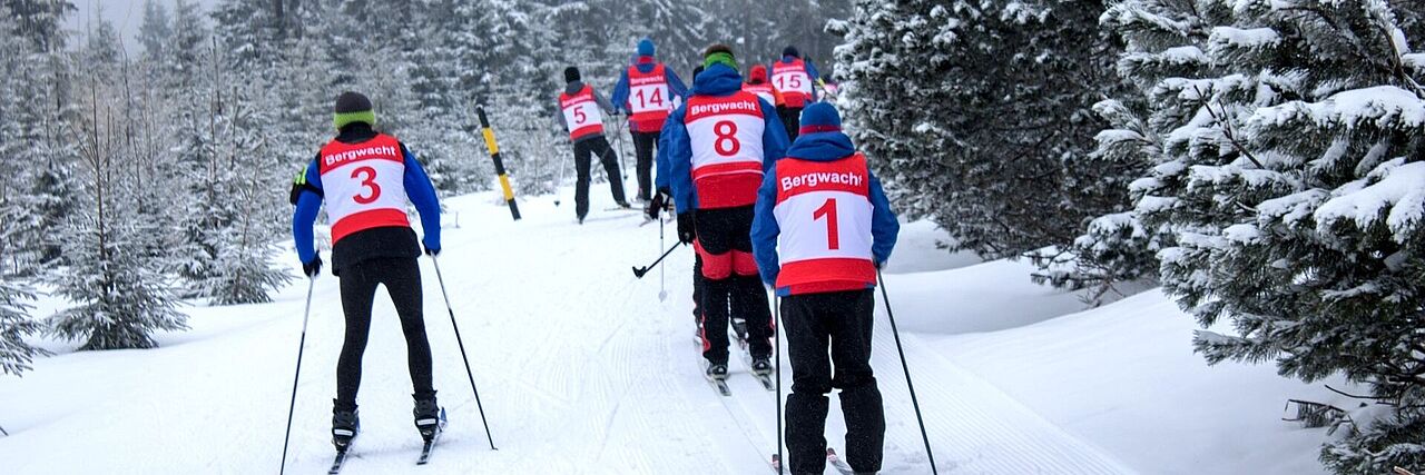 Die Ehrenamtlichen der Bergwacht trainieren ihre Skifahrt-Fähigkeiten und fahren in großer Gruppe durch einen Wald.